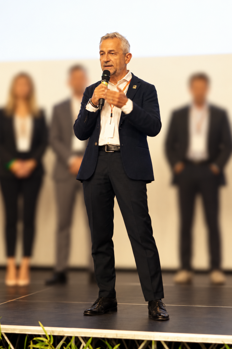 Fabio Gelmetti sul palco con microfono ad archetto, durante un incontro professionale.